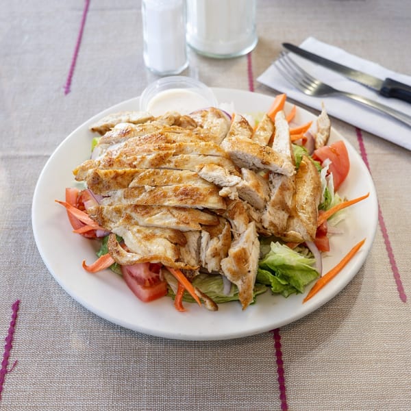Grilled chicken salad with lettuce, tomatoes, onions, and carrots, served with dressing.