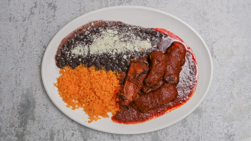 A white plate with red rice, black beans topped with cheese, and meat in red sauce.