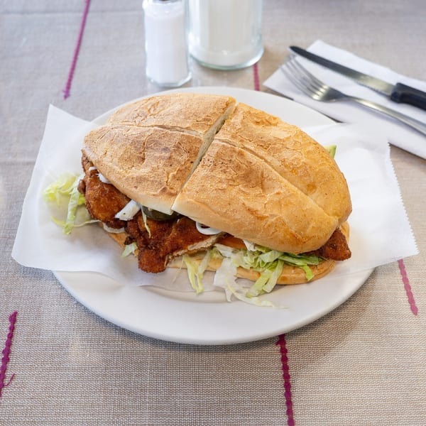 A large fried chicken sandwich, cut in half, with lettuce, tomato, and onions on a white plate.
