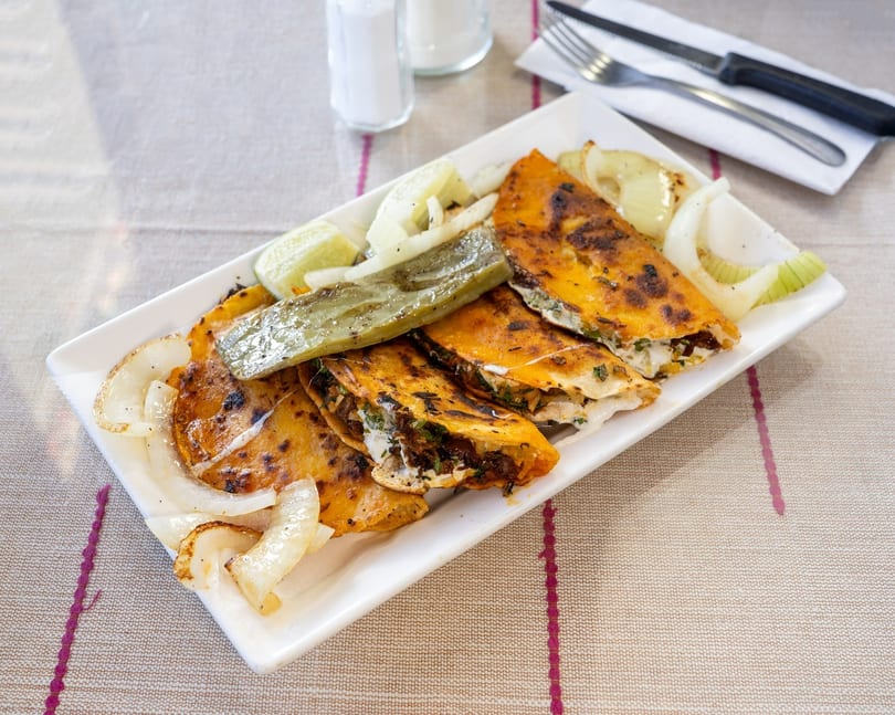 Grilled quesadillas with onions, lime, and green chili on a white rectangular plate.