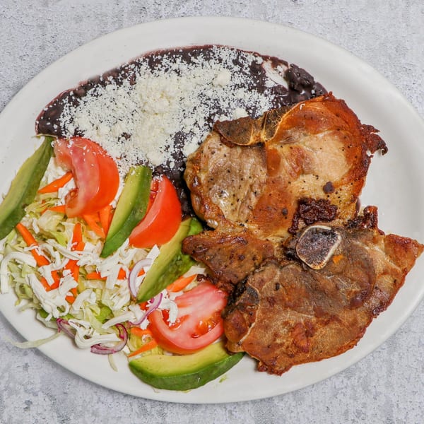 Two grilled pork chops with black beans, shredded cheese, and a side salad with avocado and tomato.