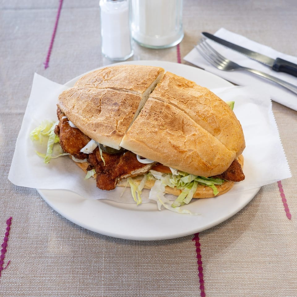 A large fried chicken sandwich, cut in half, with lettuce and onions on a white plate.