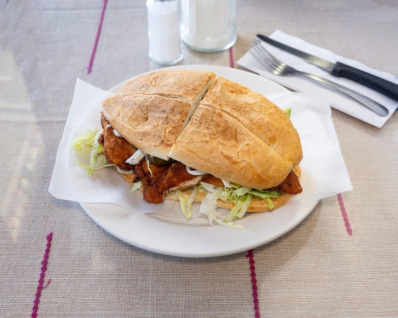 A large fried chicken sandwich, cut in half, with lettuce and onions on a white plate.