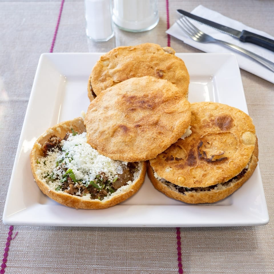 Four golden-brown sopes with various fillings, one topped with crumbled cheese and cilantro.
