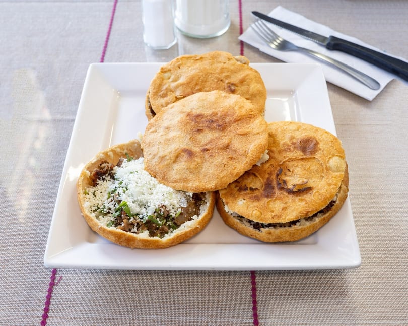 Four golden-brown sopes with various fillings, one topped with crumbled cheese and cilantro.