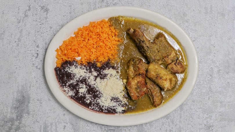 Plate of chicken in green sauce with orange rice and black beans topped with cheese.