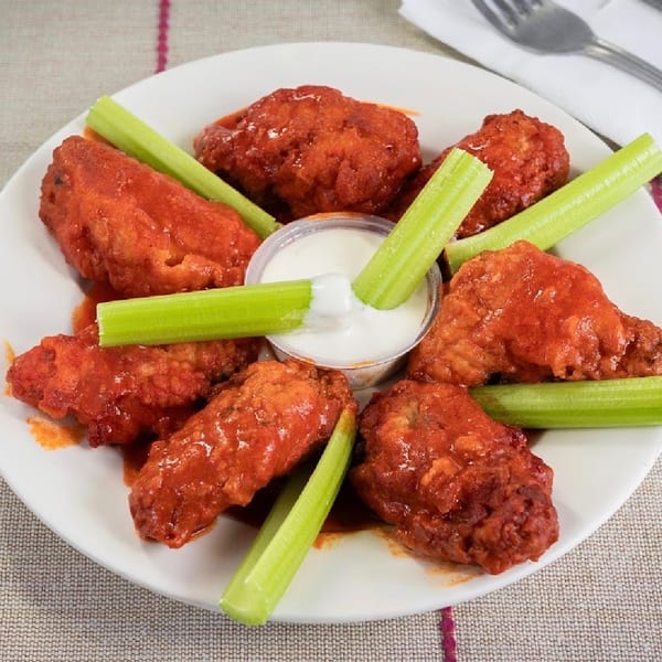 A plate of buffalo wings with celery sticks and a side of ranch dressing.