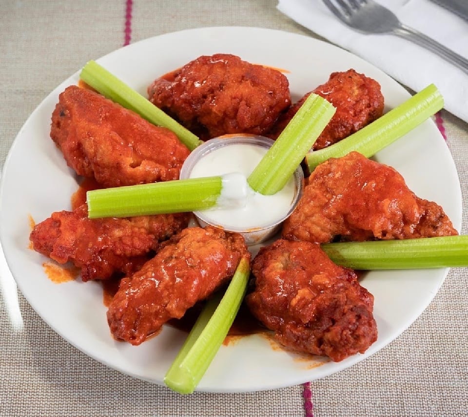 A plate of buffalo wings with celery sticks and a side of ranch dressing.