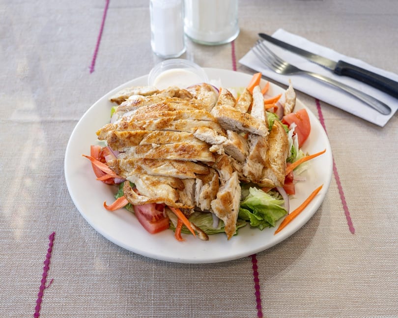 Grilled chicken salad with lettuce, tomatoes, onions, carrots, and dressing on a white plate.