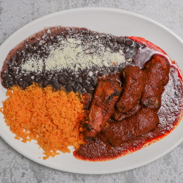 A plate of Mexican food with red rice, black beans topped with cheese, and meat in red sauce.