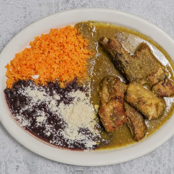 Plate of chicken in green sauce with orange rice and black beans topped with cheese.