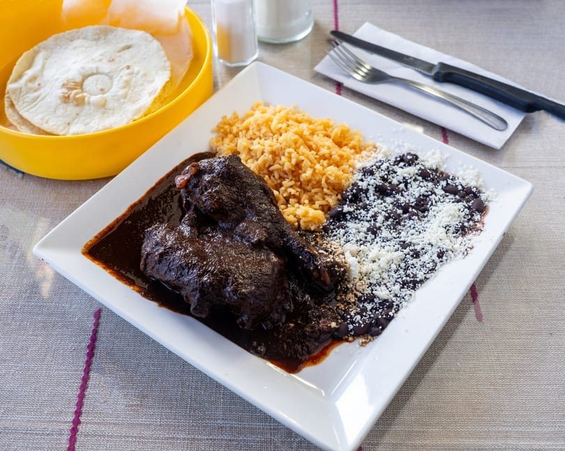 Chicken mole with rice, black beans, and crumbled cheese, served with tortillas.