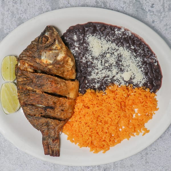 Fried fish with lime wedges, black beans topped with cheese, and orange rice on a white plate.